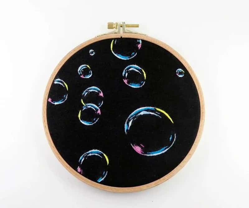 Embroidery hoop with black fabric and colorful soap bubbles design.