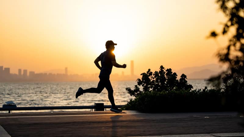 A person running along a waterfront at sunset with city skyline in the background.