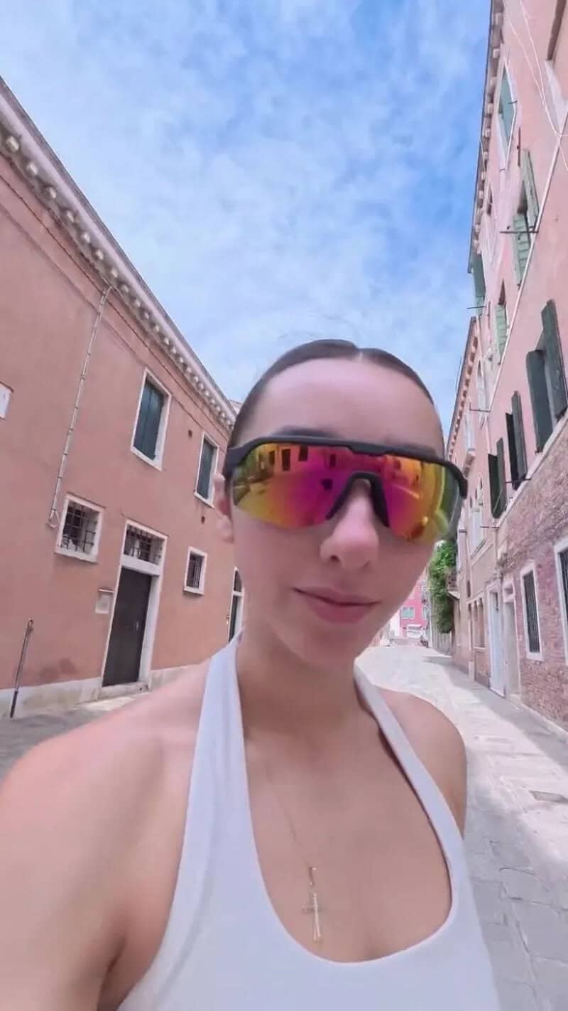 Young woman with sunglasses taking selfie in a narrow Venice street.