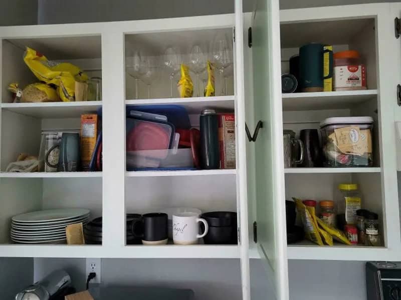Open kitchen cabinet with snacks, mugs, and kitchen items inside.