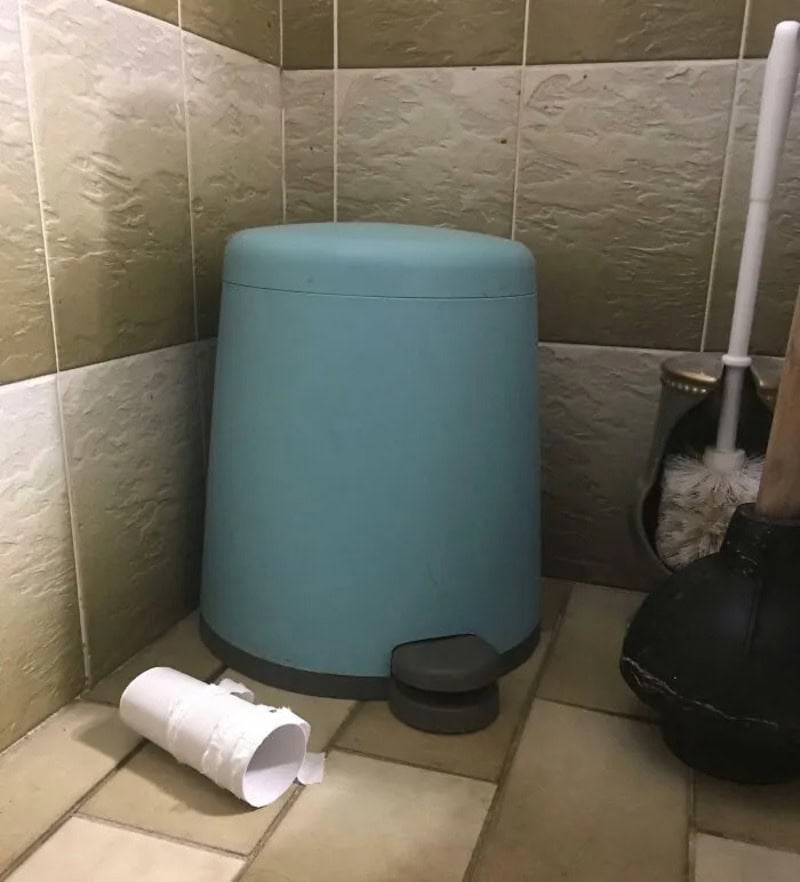 Blue trash can with a black pedal in a tiled bathroom corner.