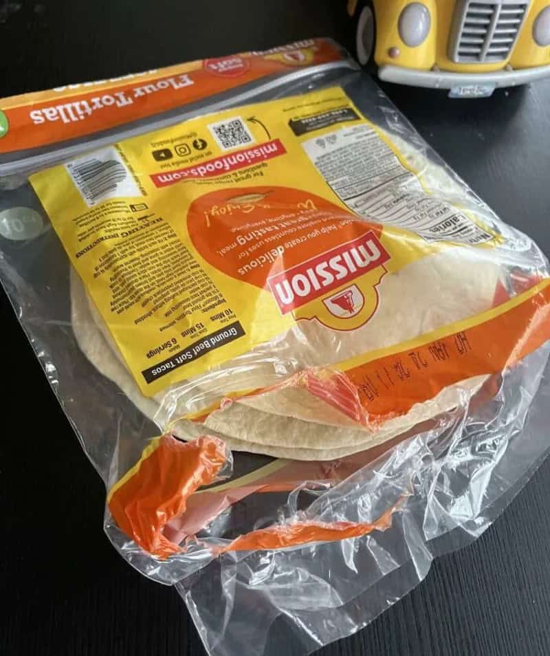 An unopened package of Mission flour tortillas on a black surface.