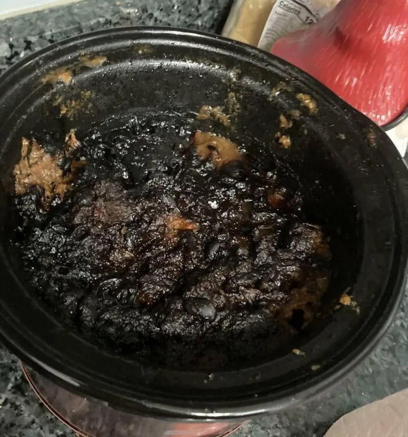 Burnt slow cooker with blackened food inside, on a kitchen counter.