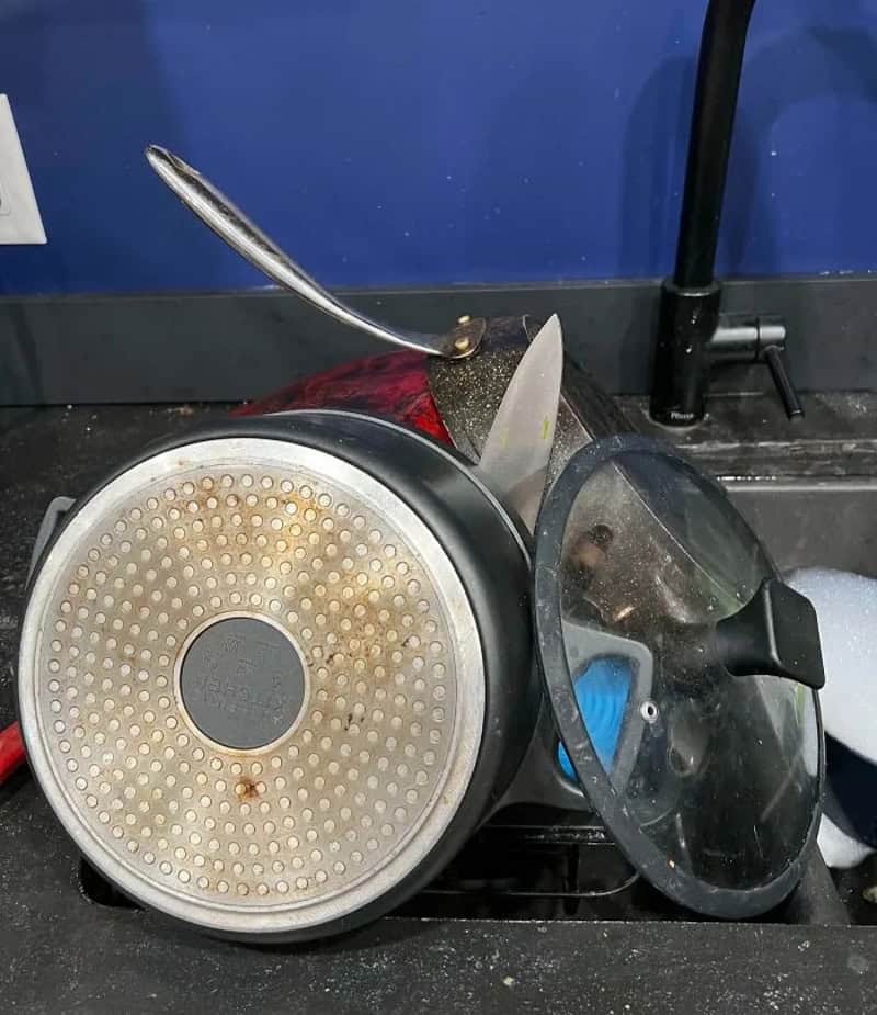 Frying pan, lid, and spatula on a black stove with a blue wall background.