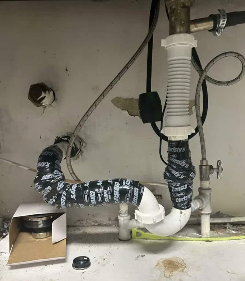 Clogged kitchen sink pipe with black tape and a cardboard box nearby.
