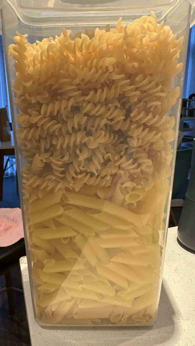 Clear container filled with different types of uncooked pasta.