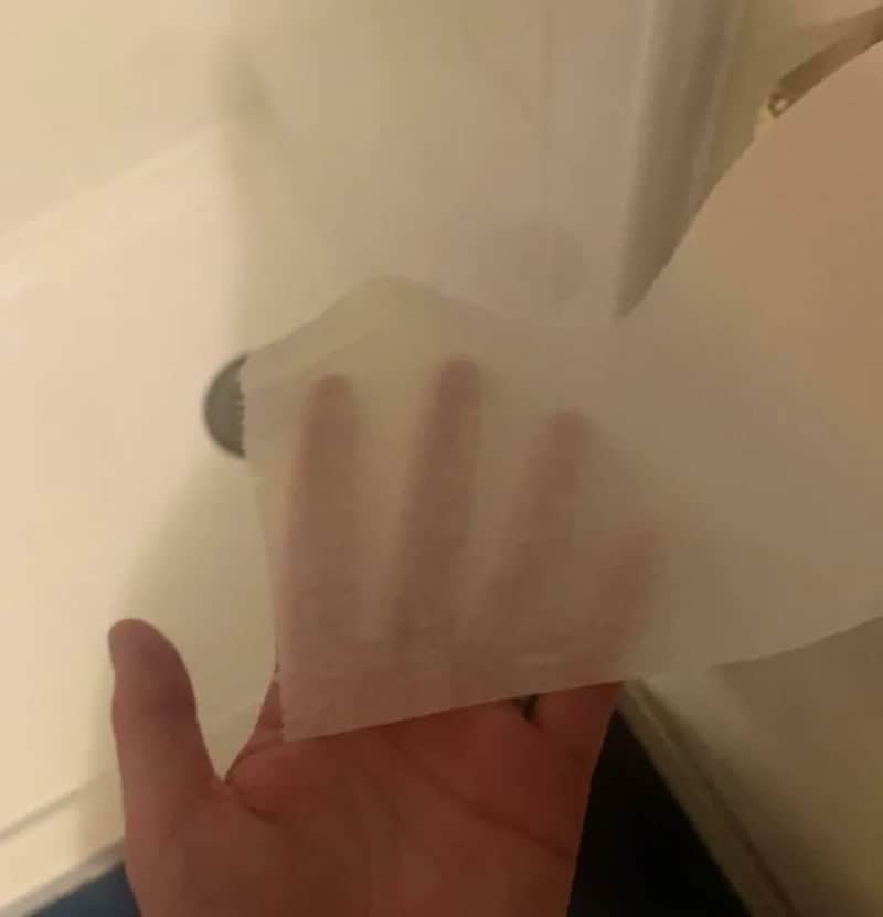 Person peeling a sticker or paper from a surface, with a hand visible.