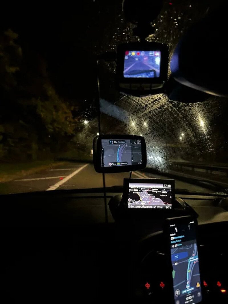Nighttime car interior with multiple GPS devices and rain on windshield.