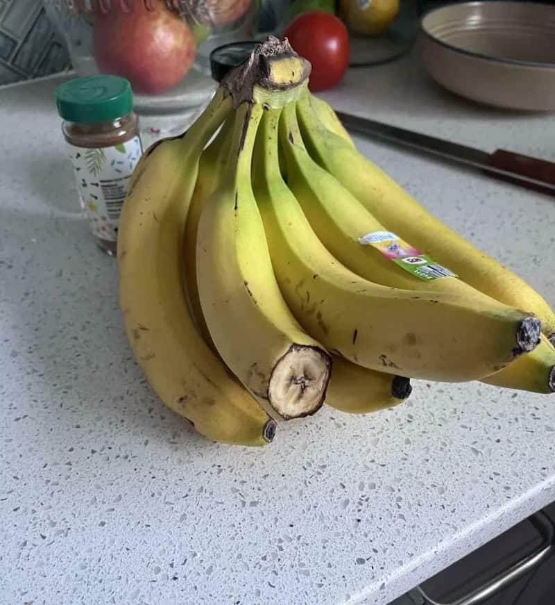 Bunch of bananas on a kitchen counter with apples and spices in the background.
