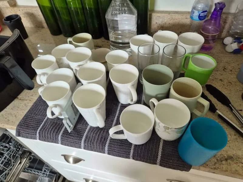 Collection of used coffee mugs and glasses on a kitchen counter.