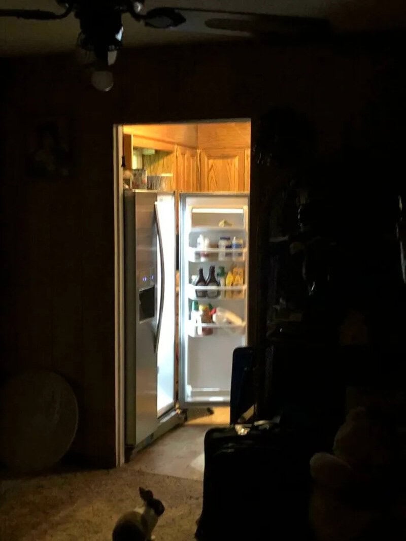 Open refrigerator in a dark room with light inside, showing food and drinks.
