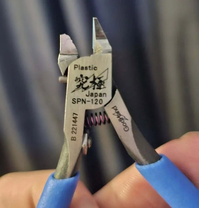 Cutting pliers gripping a plastic object with Japanese text and a spring.