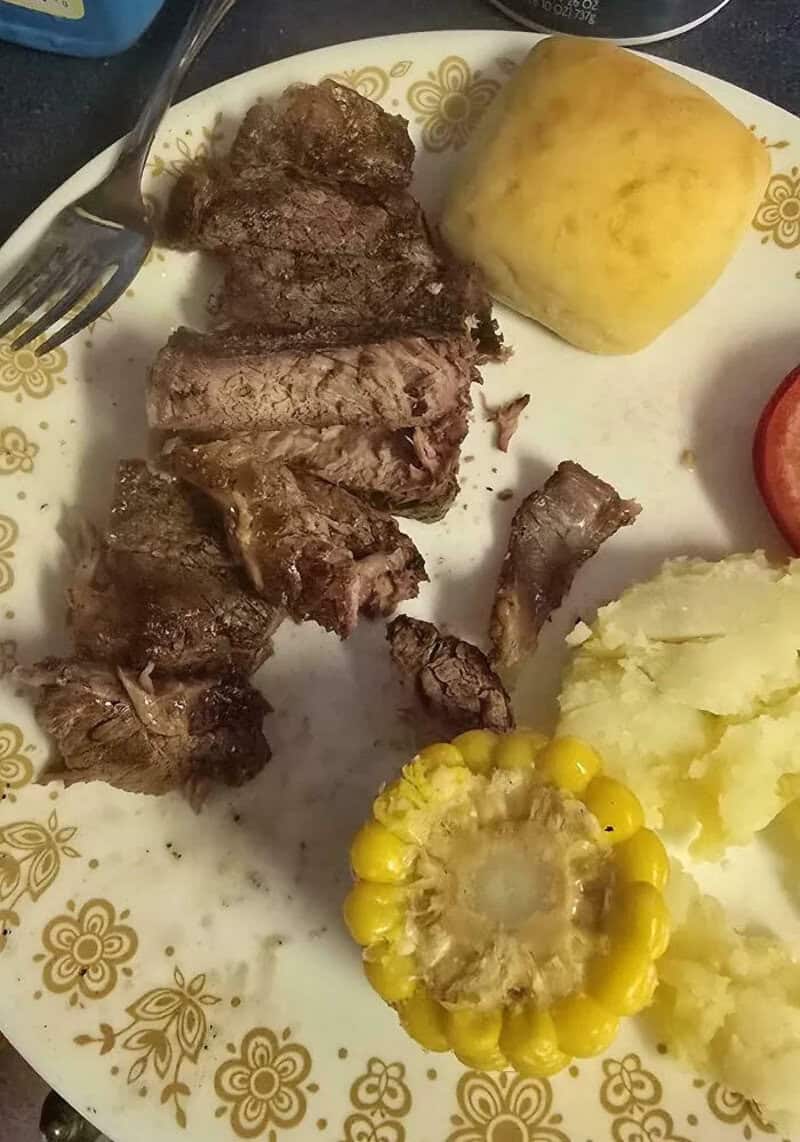 Steak, mashed potatoes, corn on the cob, bread, and tomato on a decorative plate.