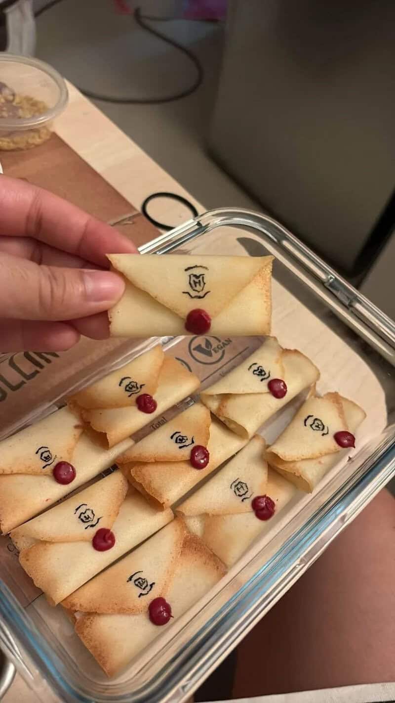 Miniature cookies with red berries and a logo, in a glass container.