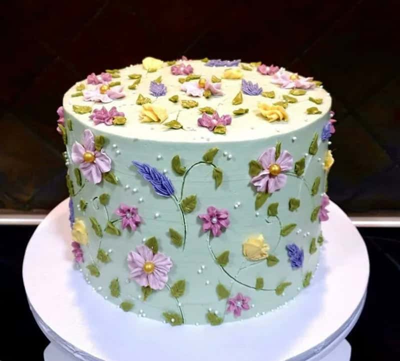 Decorated cake with pastel flowers and green leaves on a white base.