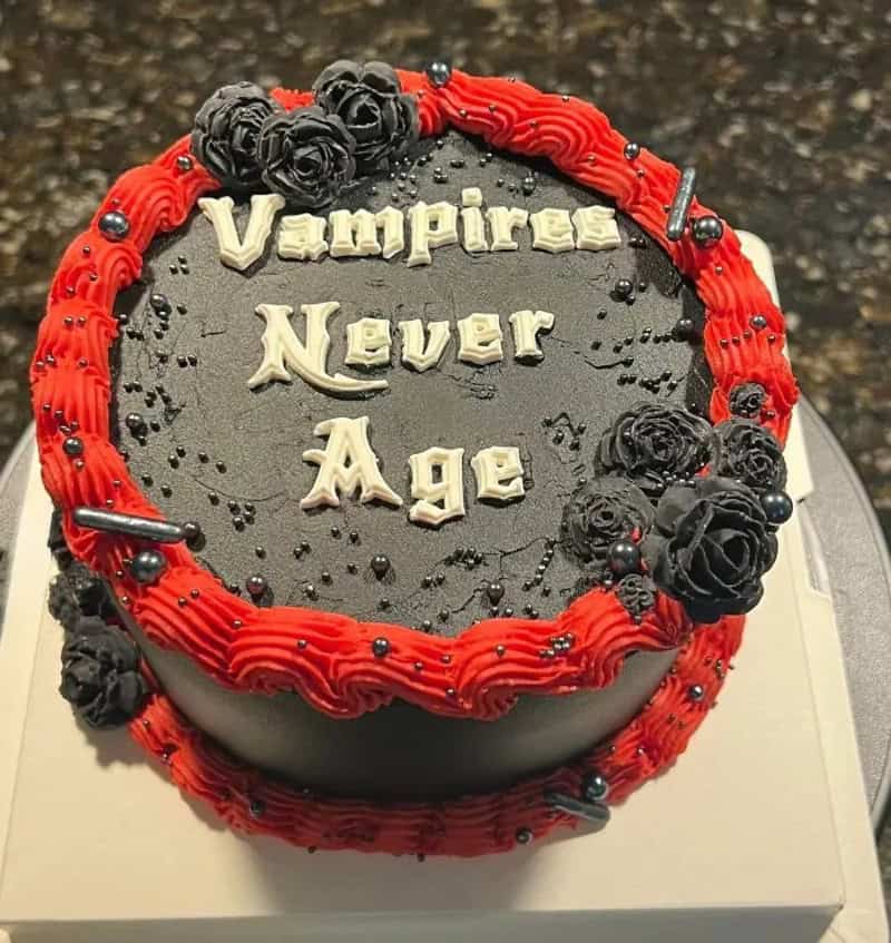 Black and red decorated cake with the words 'Vampires Never Age' on top.