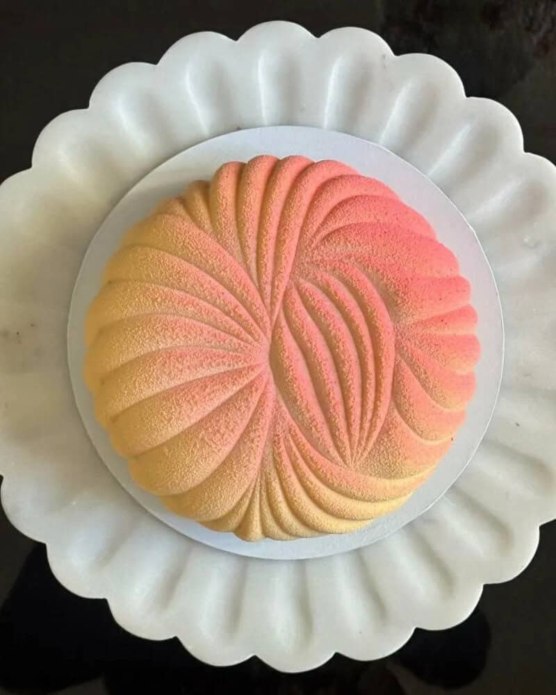 Colorful, swirled dessert with pink and yellow hues on a white scalloped plate.