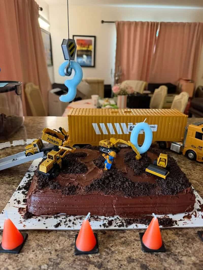 Construction-themed cake with toy trucks and a crane, decorated with orange cones.