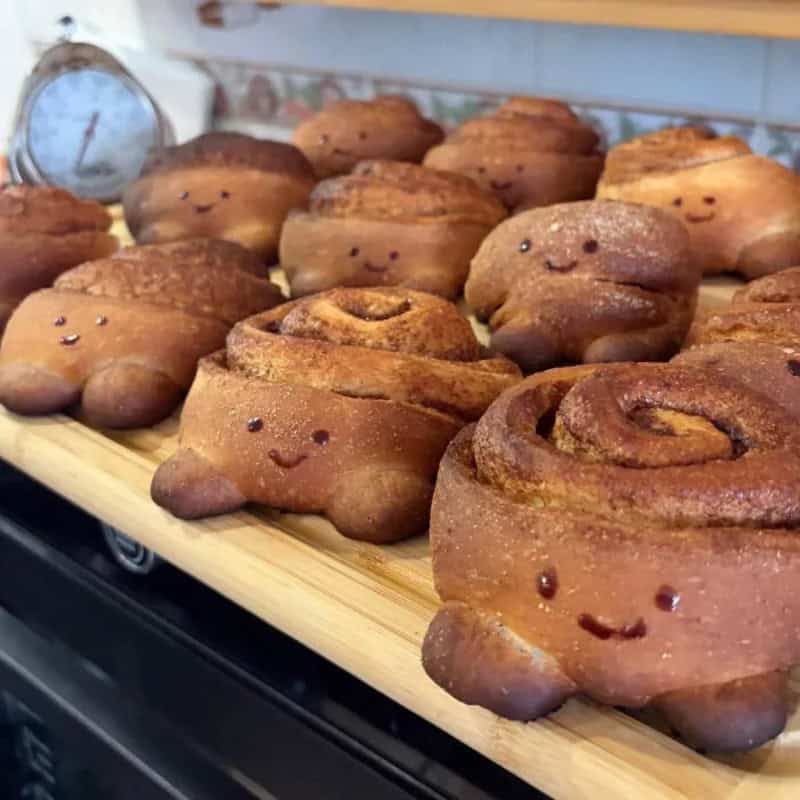 Cute cinnamon rolls with smiling faces on a wooden tray.