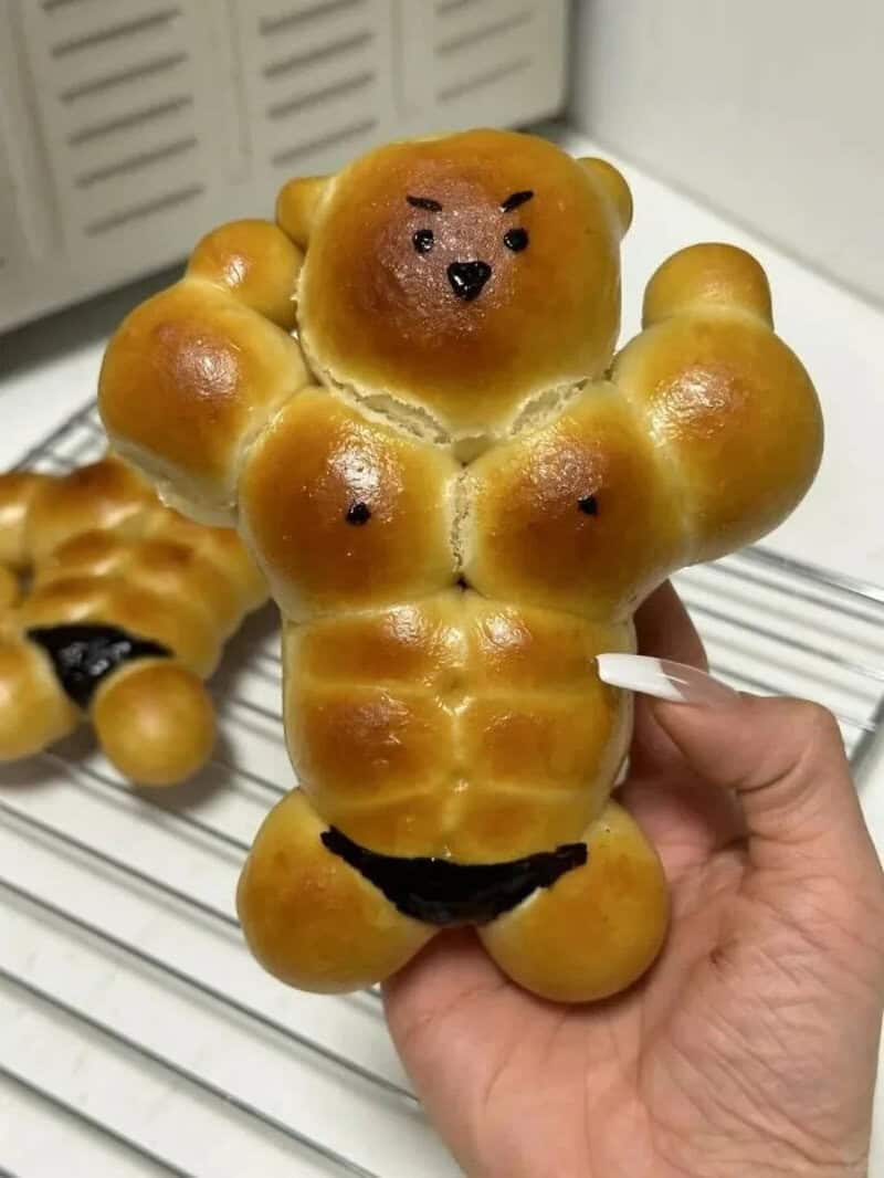 Bread shaped like a muscular bear with a face, arms, and abs, held in hand.