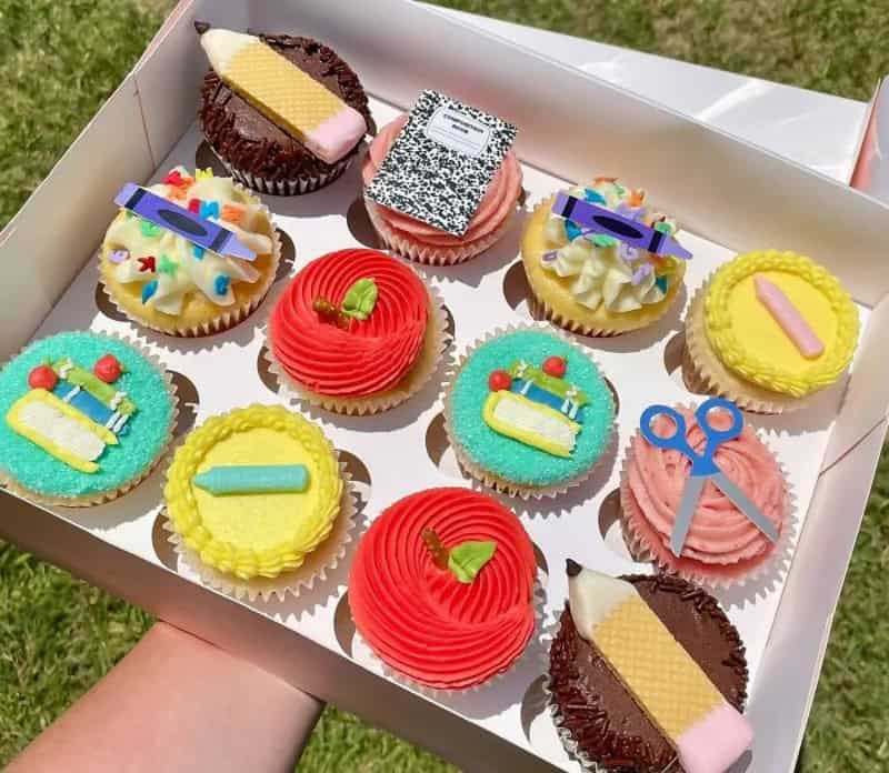 Colorful cupcakes with various decorations in a box, outdoors.