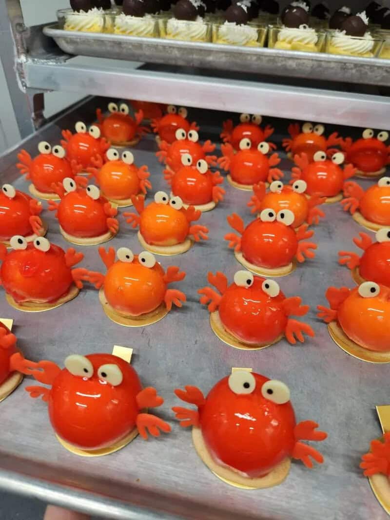 Crab-shaped desserts with orange glaze, eyes, and claws on a tray.