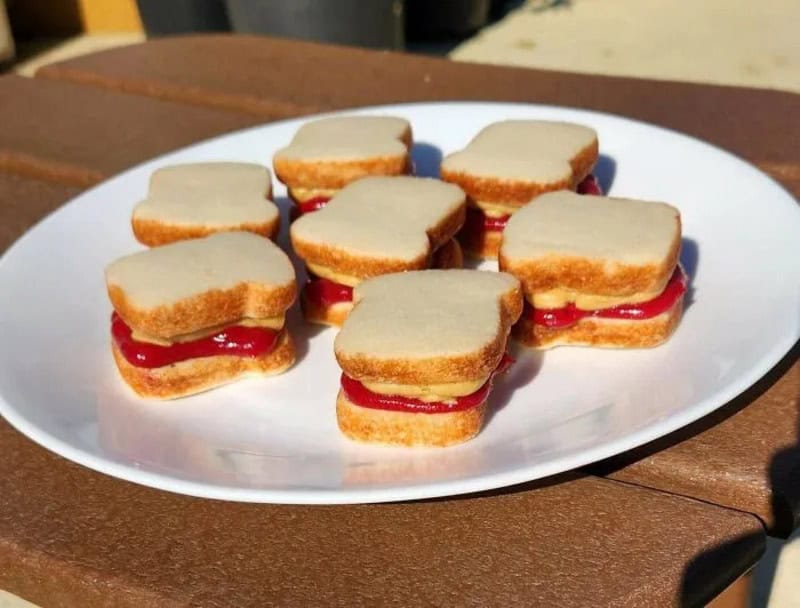 Mini sandwiches with white bread and red jam on a white plate.