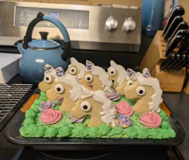 Unicorn cookies on a green frosting base with a blue teapot in the background.