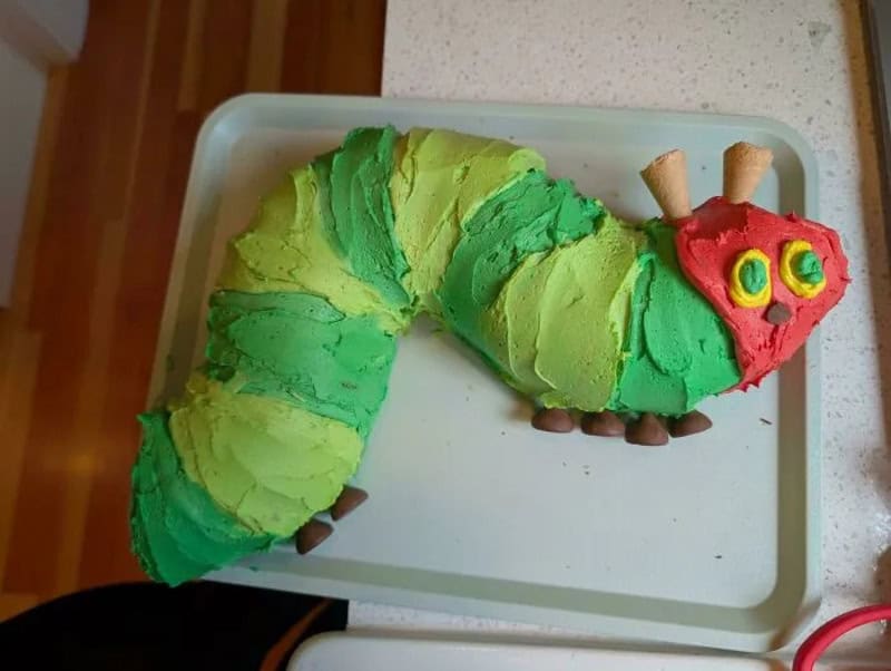 Colorful caterpillar cake with green, red, and yellow icing, on a white tray.