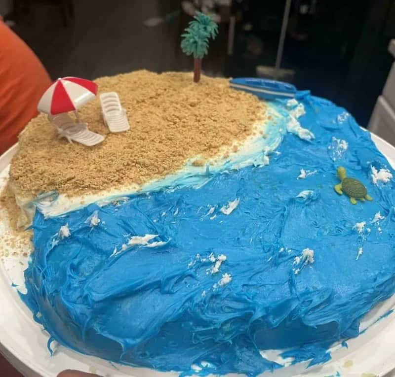 Beach-themed cake with blue icing, sand, umbrella, and turtle decorations.