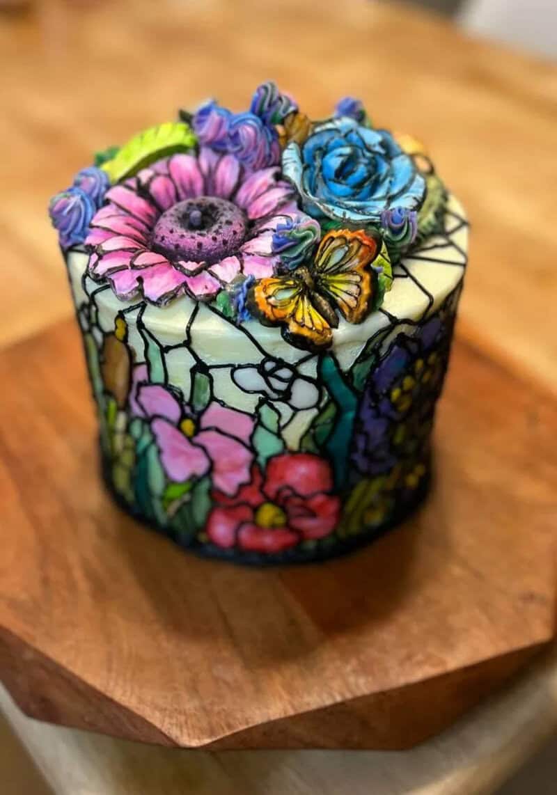 Colorful stained glass-style cake with flowers and butterflies on top.
