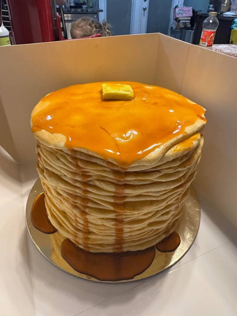 Stack of pancakes with butter and syrup, in a box.