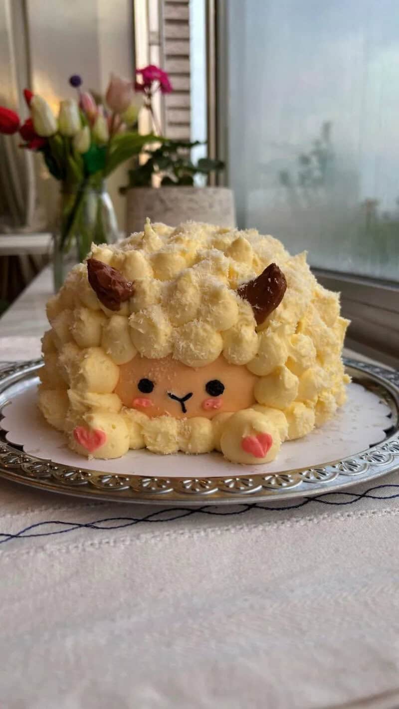 Cute sheep-shaped cake with cream, chocolate horns, and pink cheeks.