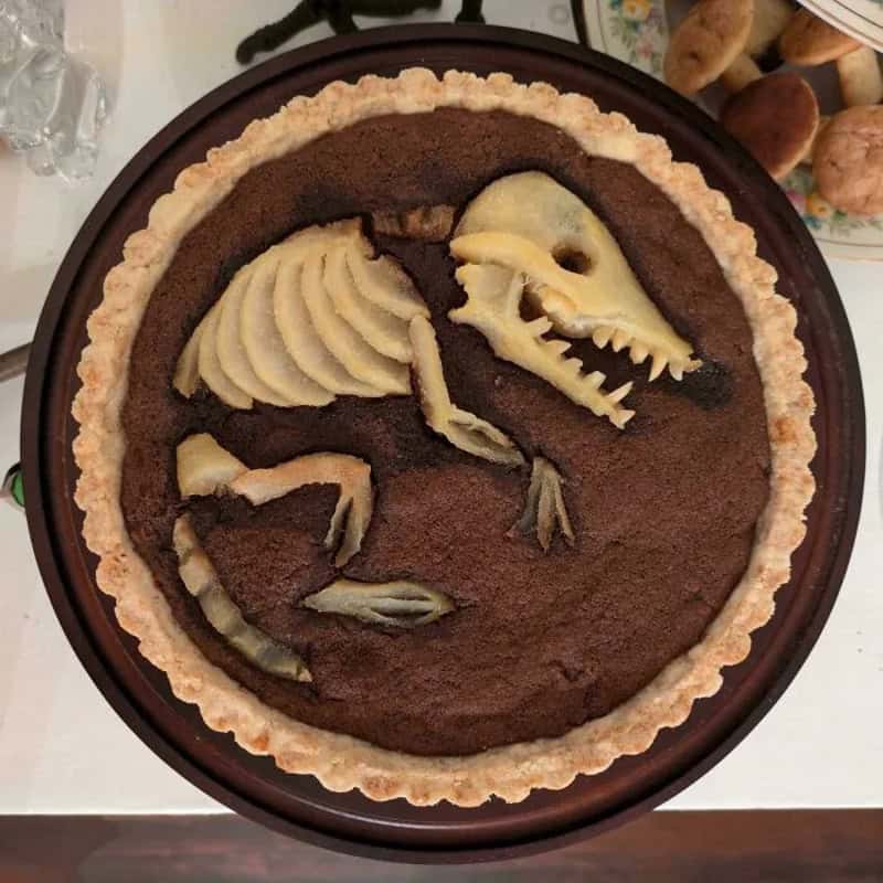 Chocolate tart with dinosaur skeleton decorations made of fruit and pastry.