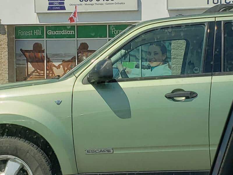 Smiling woman in car with a large poster of a woman in the background.