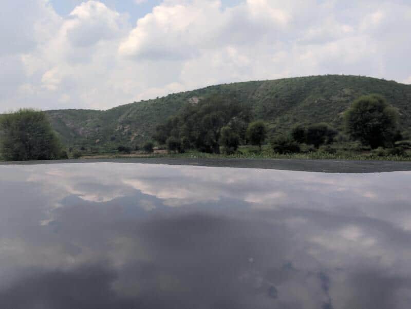 View of a landscape with hills, trees, and cloudy sky, reflected on a shiny surface.