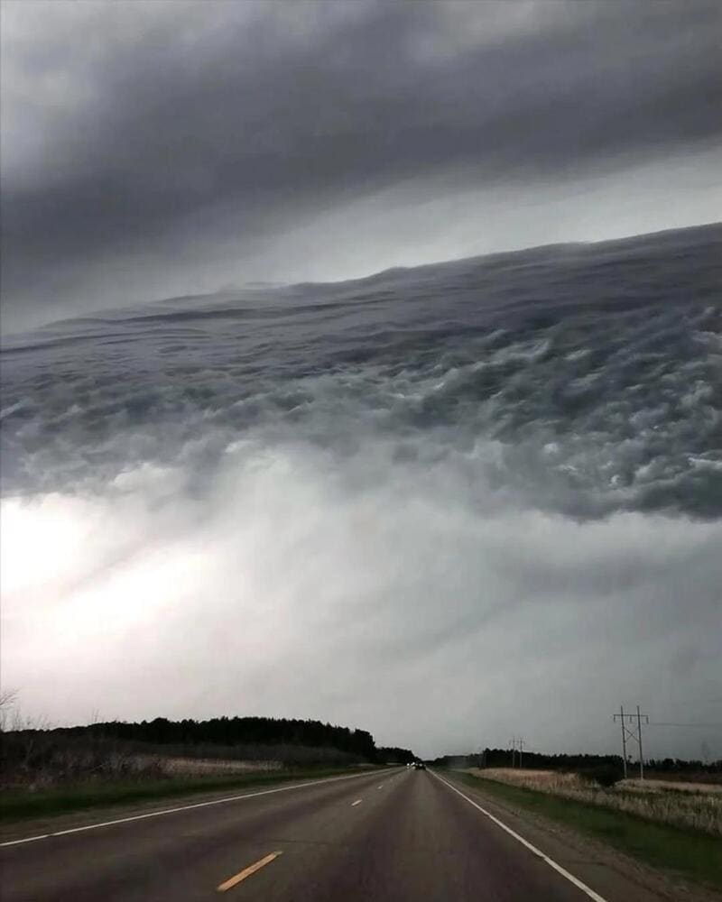 Stormy sky with dark clouds over a straight road and open fields.