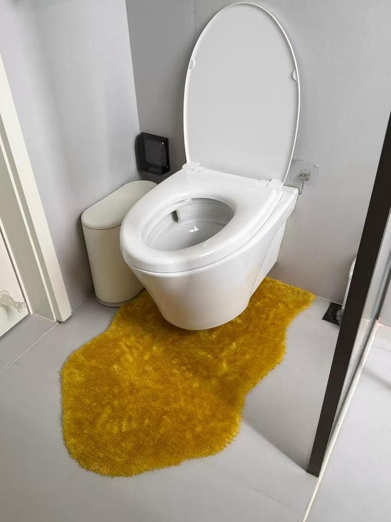 Toilet with yellow rug and trash bin in a modern bathroom.