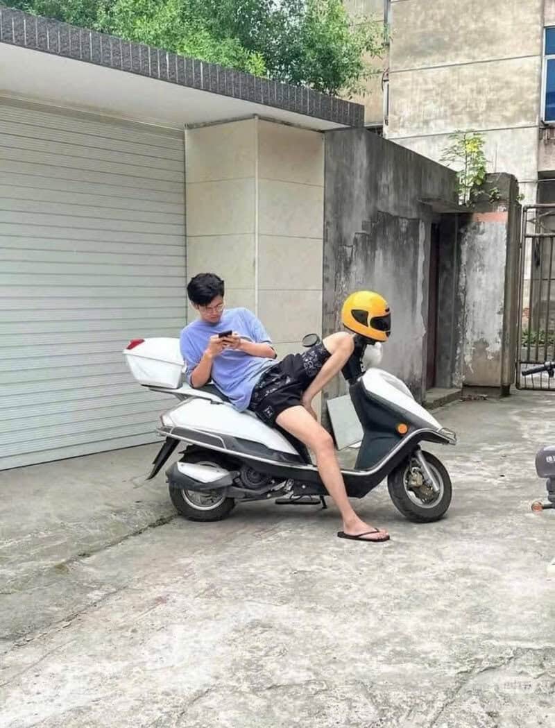 Young man on scooter with helmet, looking at phone, in front of garage door.