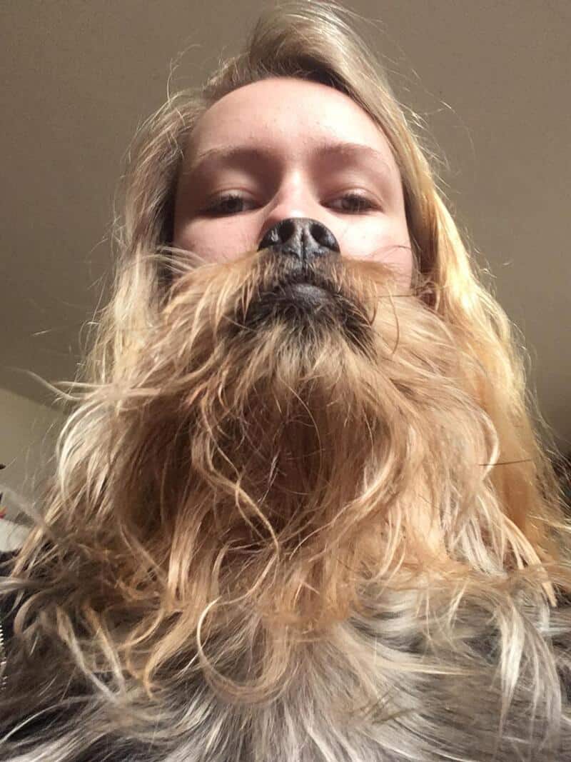 Person with a dog's face covering their mouth and nose, looking down at the camera.
