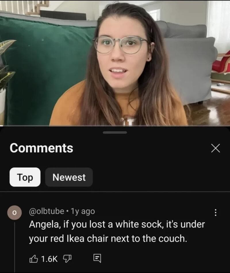 Angela with glasses looks surprised, sitting on a green couch.