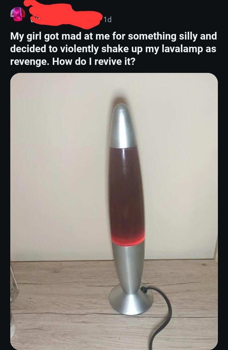 Lava lamp with a red glow, standing on a wooden surface against a white wall.