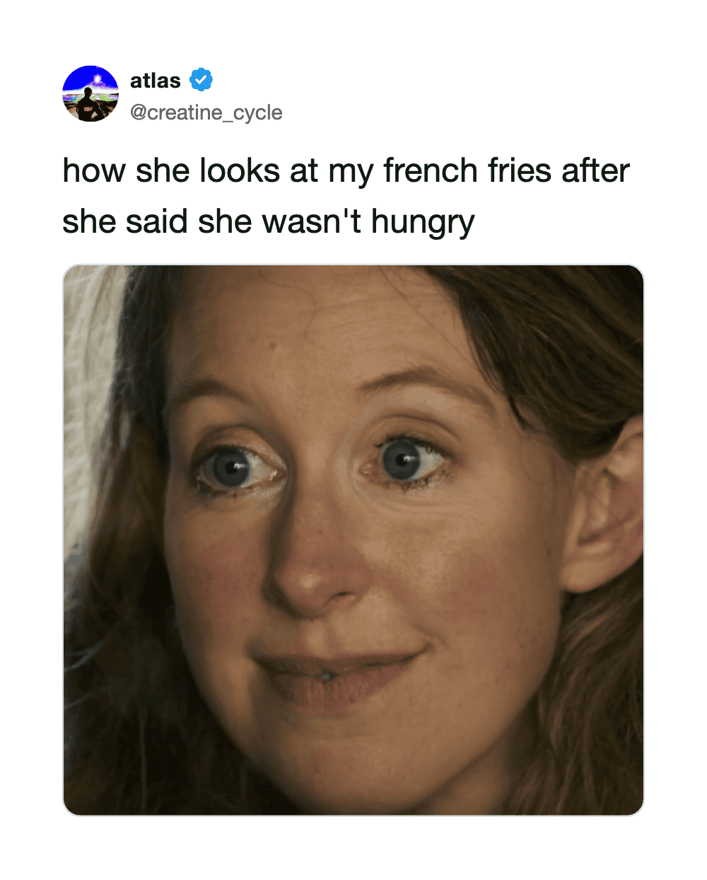 Woman with wide eyes looking at French fries, smiling slightly.