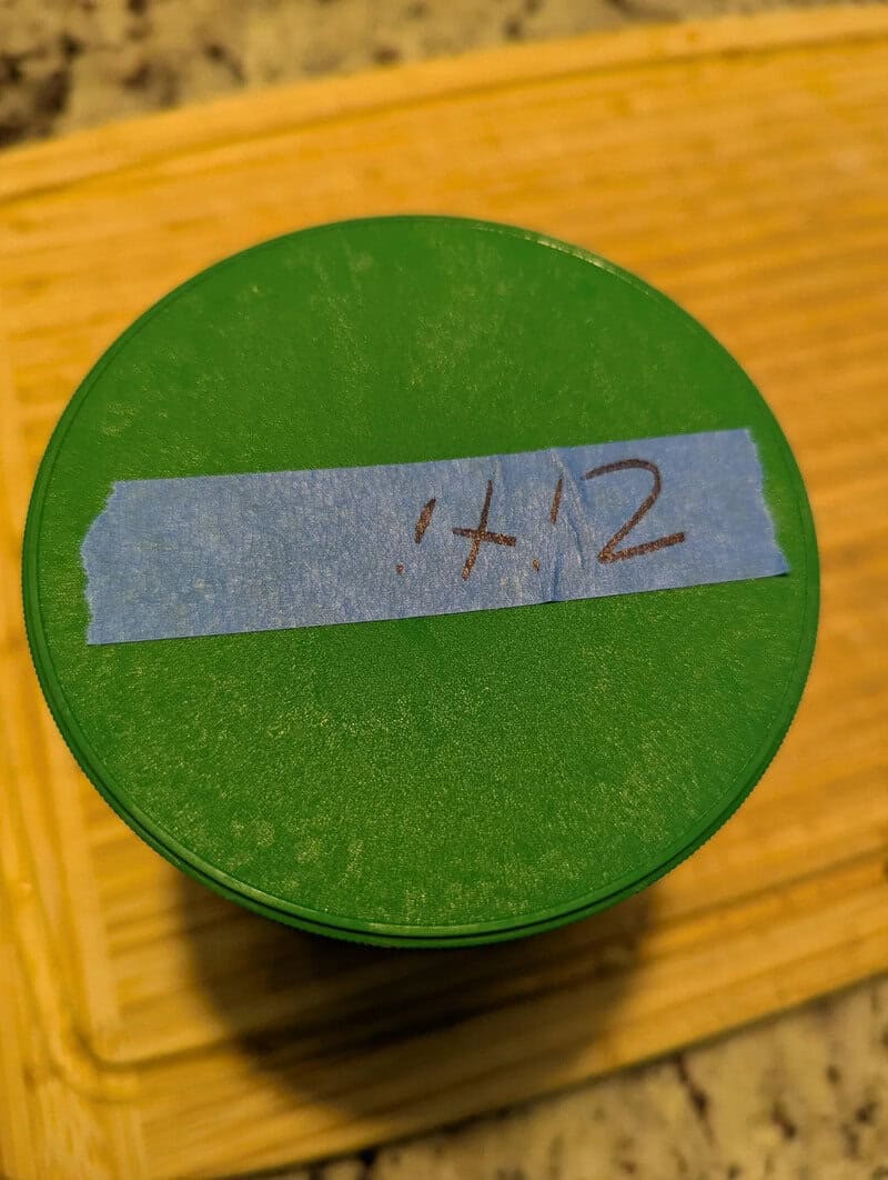Green container with blue tape labeled '+12' on a wooden surface.