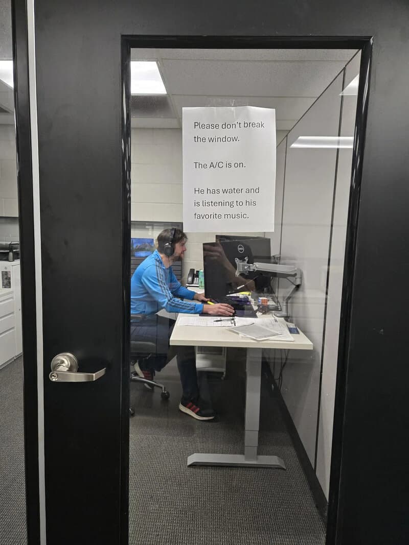 Person working at a desk in a small office with a sign on the window.