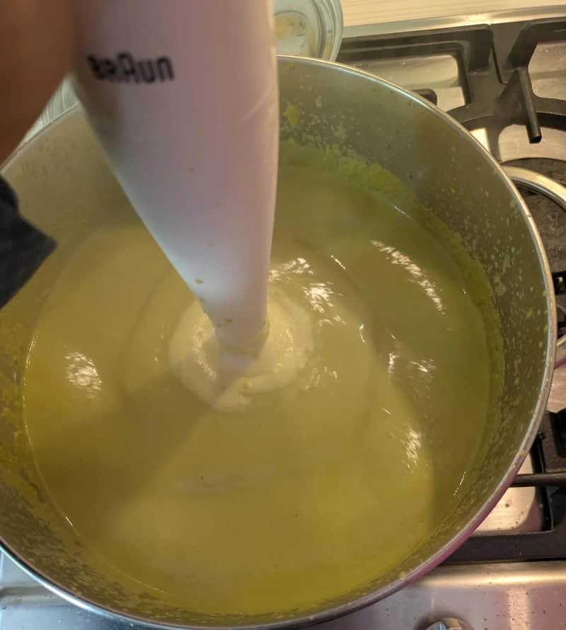 Blender blending yellow mixture in a pot on stove.