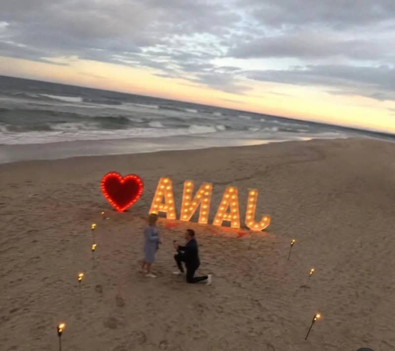 Beach scene with illuminated 'LOVE' and 'ANNA' signs at sunset.