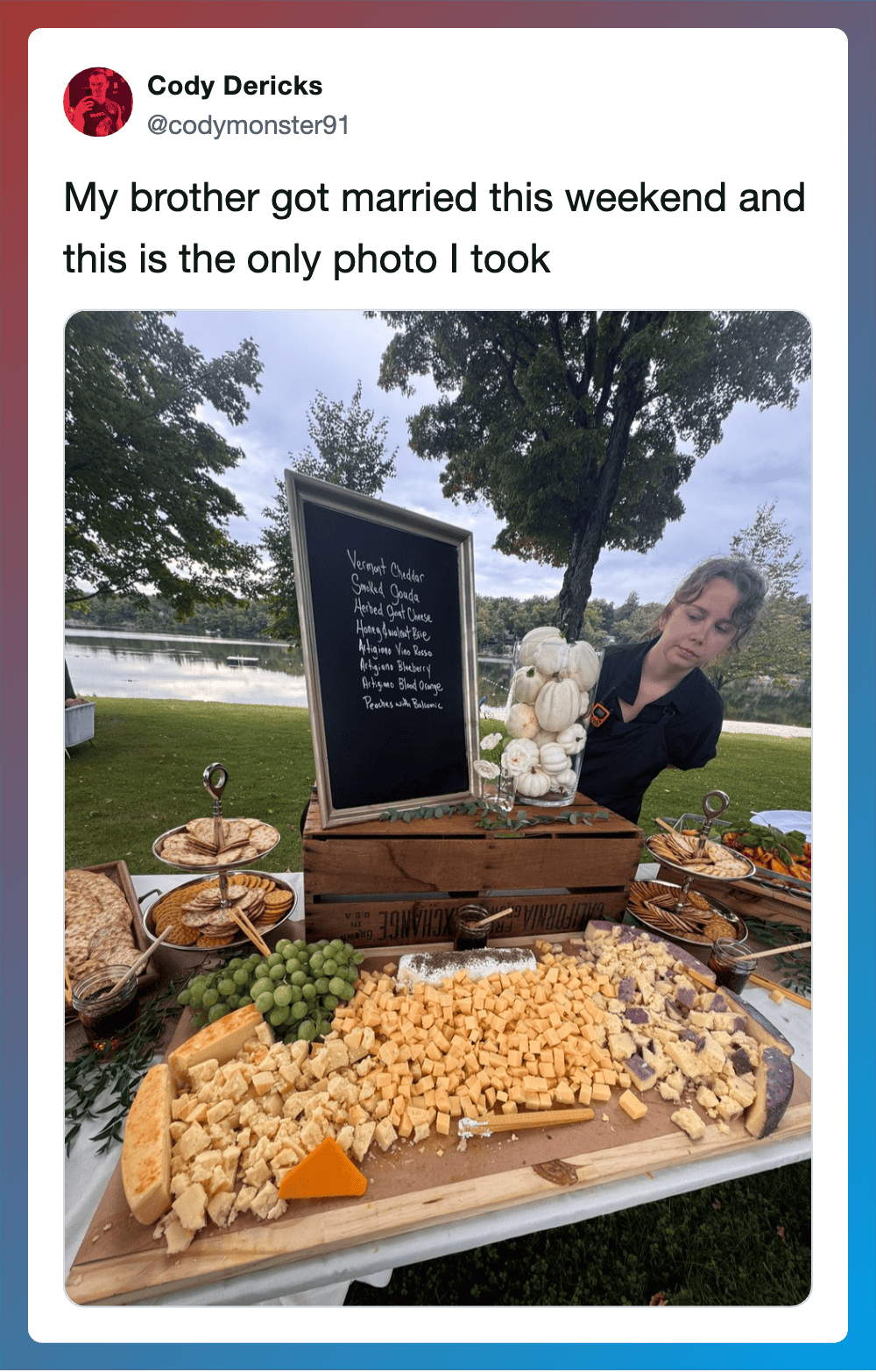 Photo of a woman at a wedding reception outdoors with cheese, grapes, and a chalkboard sign.