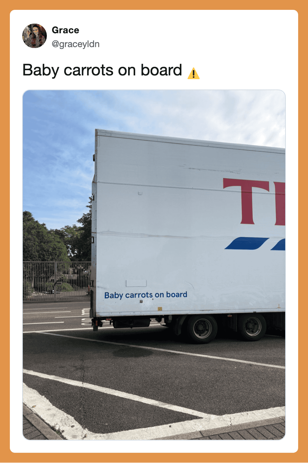 Baby carrots on board sign on a truck with blue sky and trees in background.