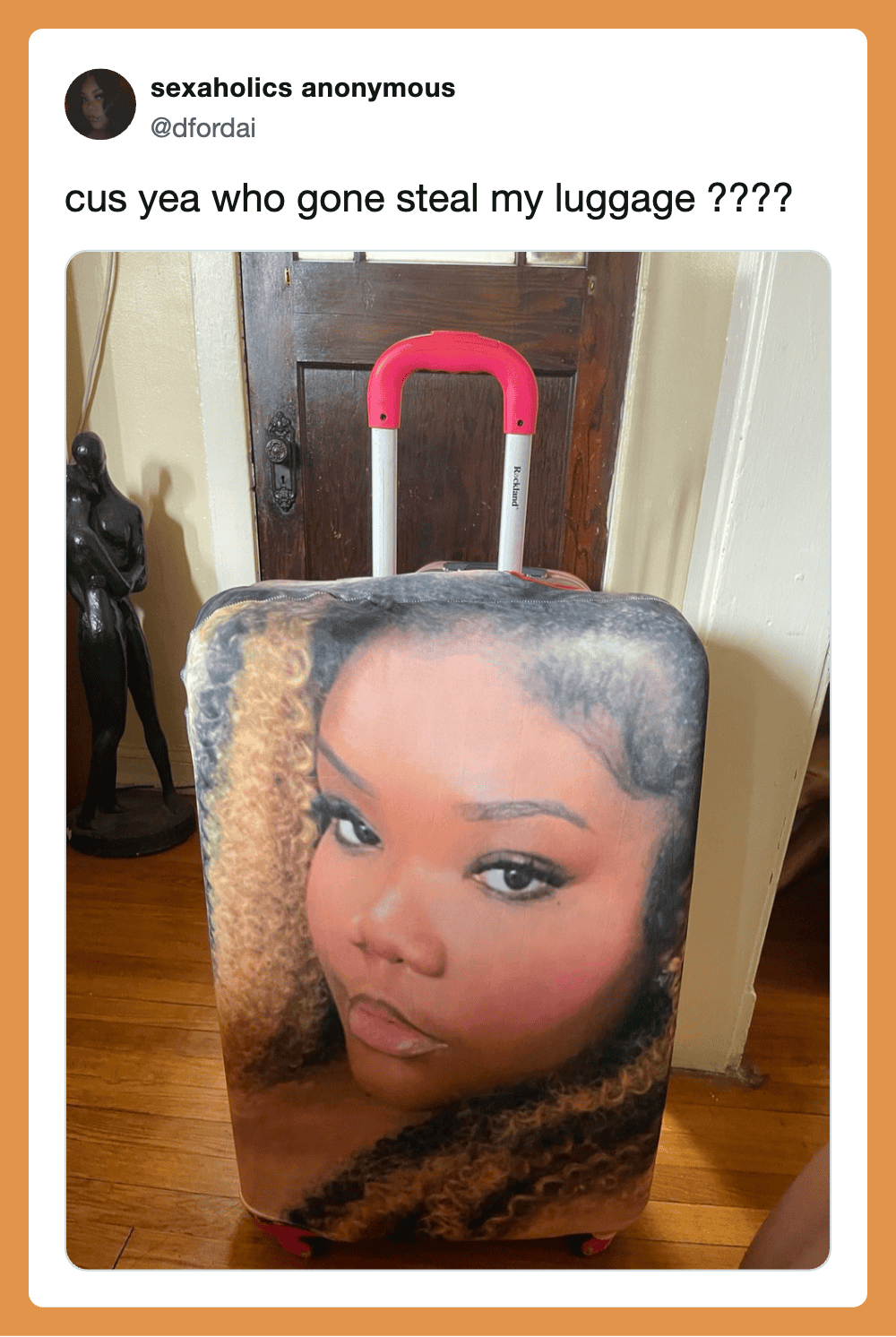 Luggage with a woman's face printed on it, pink handle, in a home setting.